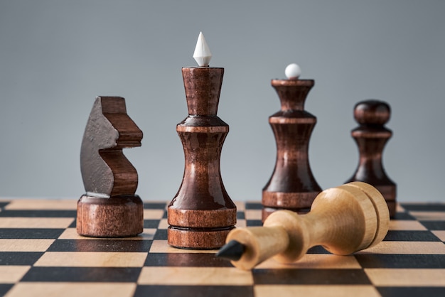 Wooden chess pieces on a chessboard, the white king lies in front of the black pieces, the concept of strategy, planning and decision making