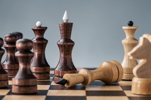 Wooden chess pieces on a chessboard, the white king lies in front of the black pieces, the concept of strategy, planning and decision making