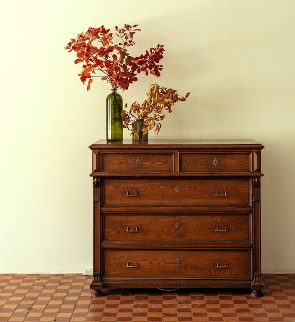 Wooden chest of drawers with floral branches in vase