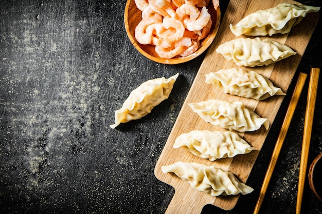 A wooden chopping board with dumplings and shrimps on it.