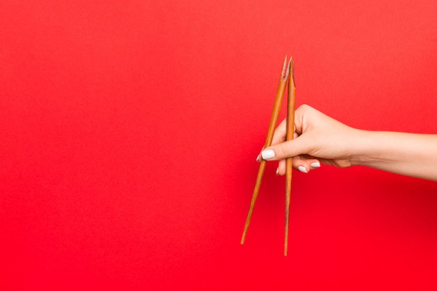 Wooden chopsticks holded with female hands on red background. Ready for eating s with empty space