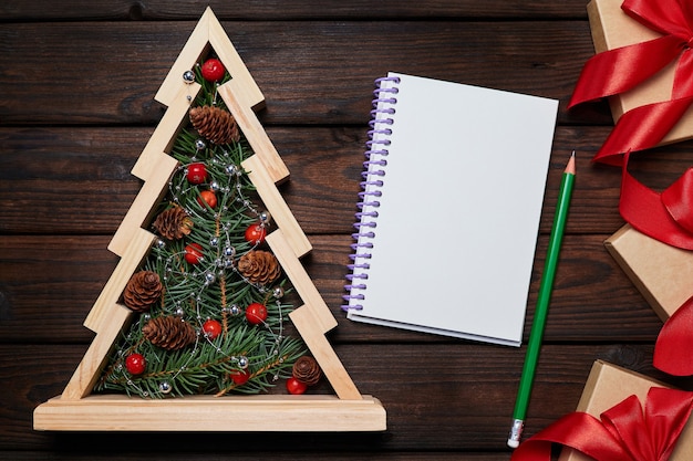 Wooden christmas tree with Fir branches inside gift boxes with red ribbons and a Blank notepad