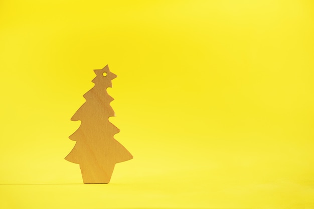 Wooden Christmas tree on yellow background with copy space. New Year party. 