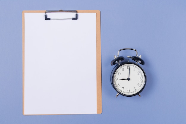 Photo of wooden clipboard with blank paper and alarm-clock on light grey background.  free space. copy space. top view.