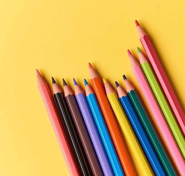 Wooden color pencils on yellow paper background, top view