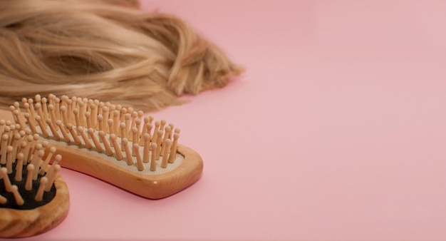 Wooden comb on the background of blonde blonde hair on a pink background with a place for text