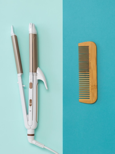 Photo wooden comb and electric hair tongs on a two-color background. hair care accessories.