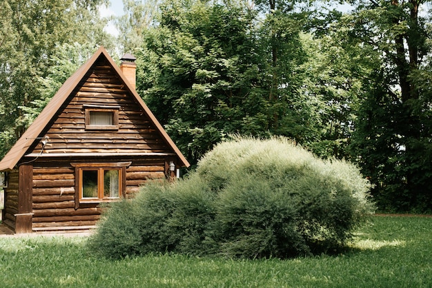 Wooden country house from a log in the forest on a sunny summer day. Exterior one storey cottage, bungalow. Tranquil rural scene.