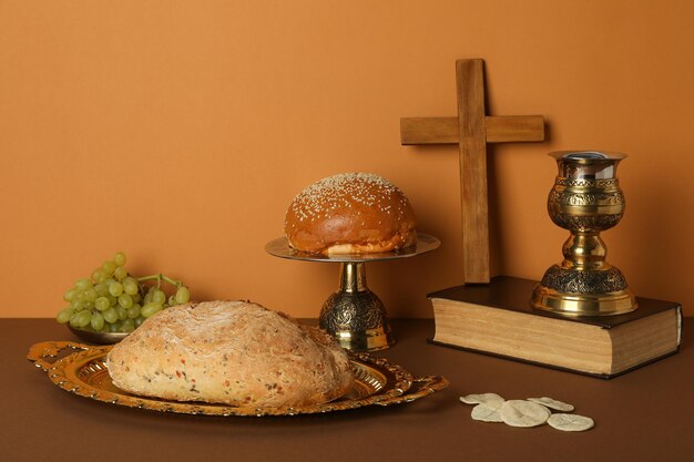 Wooden cross and cup on book bread and grapes on orange background