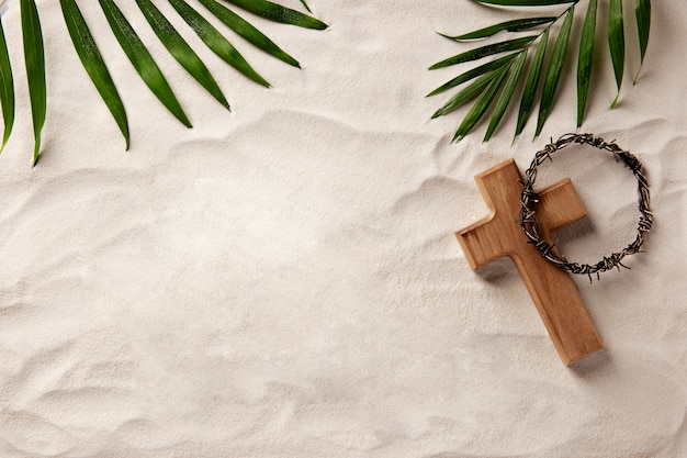 Wooden cross and leaves on sand top view