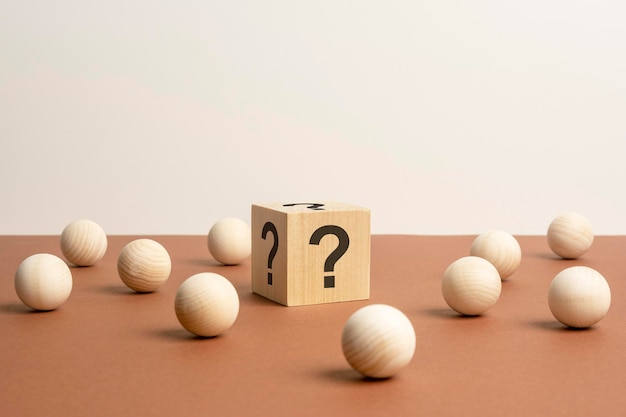 Wooden cube with a question mark surrounded by wooden balls on a brown table background