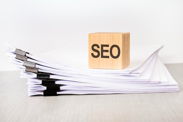 A wooden cube with a text SEO on a stack of documents grey table white background