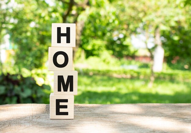 Wooden cubes are stacked vertically on a wooden table in the garden the word home is written in blac...