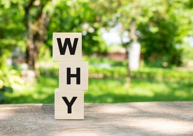 Wooden cubes are stacked vertically on a wooden table in the garden the word why is written in black...