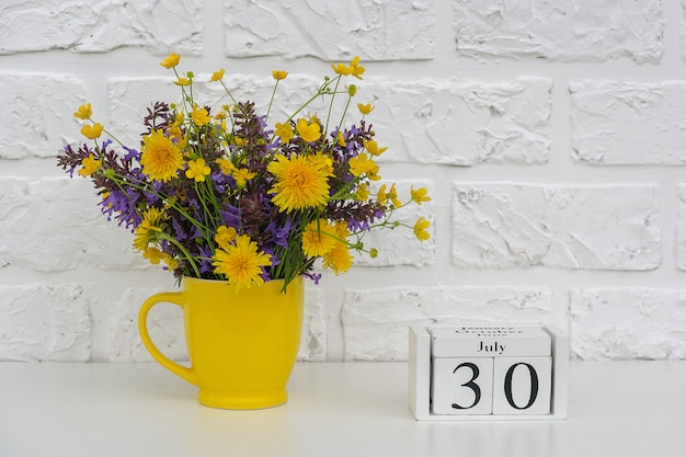 Wooden cubes calendar July 30 and yellow cup with bright colored flowers 