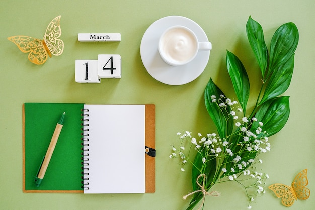 Wooden cubes calendar March 14. Notepad, cup of coffee, bouquet flowers on green background. Concept hello spring Top view Flat lay Mock up