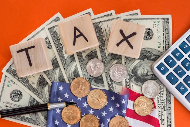 Wooden cubes tax with flag, dollar, coin and calculator on orange background