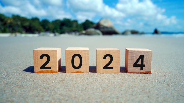 Wooden cubes with 2024 and happy new year inscription over beach sand background