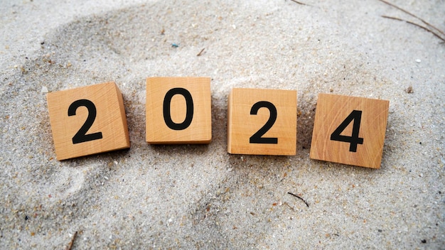 Wooden cubes with 2024 and happy new year inscription over beach sand background