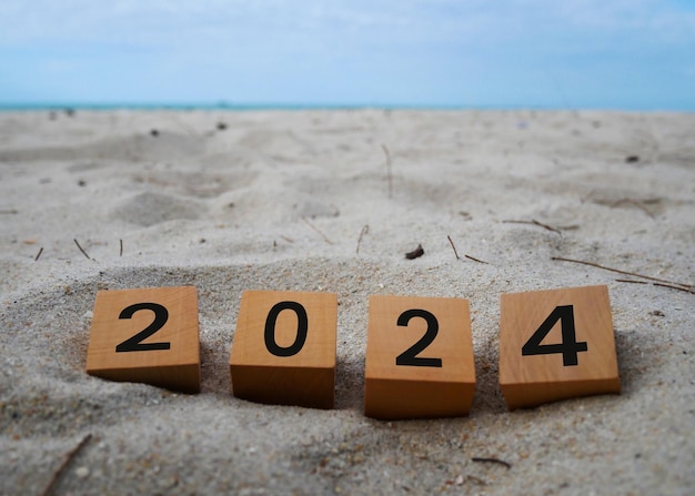 Wooden cubes with 2024 and happy new year inscription over beach sand background