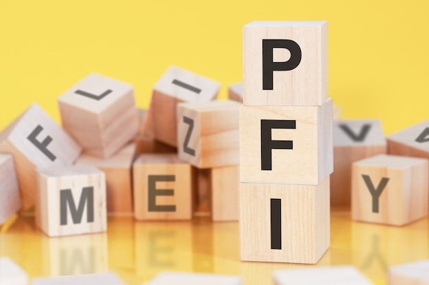 Wooden cubes with letters PFI arranged in a vertical pyramid, yellow background, reflection from the surface of the table, business concept,