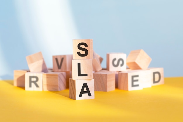 Wooden cubes with letters sla arranged in a vertical pyramid, yellow background, business concept. sla - short for service level agreement