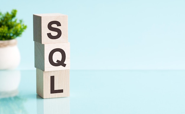 Wooden cubes with letters SQL arranged in a vertical pyramid, blue background, reflection from the surface of the table. SQL - short for Structured Query Language