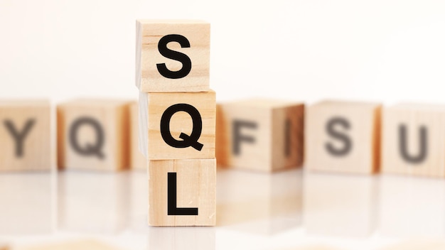 Wooden cubes with letters sql arranged in a vertical pyramid, white background, reflection from the surface of the table, business concept. SQL - short for Structured Query Language