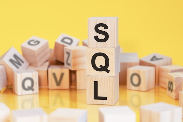 Wooden cubes with letters sql arranged in a vertical pyramid, yellow background, reflection from the surface of the table, business concept