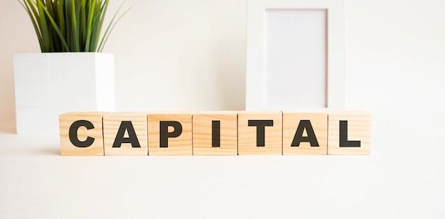 Wooden cubes with letters on a white table The word is CAPITAL