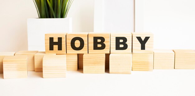 Wooden cubes with letters on a white table. The word is HOBBY. White background with photo frame, house plant.