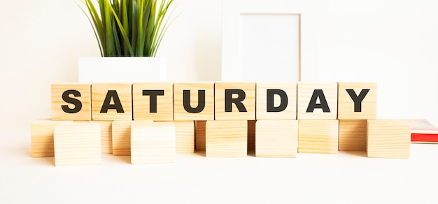 Wooden cubes with letters on a white table. the word is saturday. white background with photo frame, house plant.