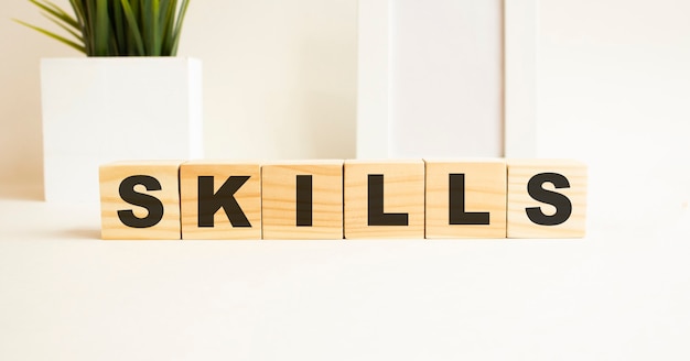 Wooden cubes with letters on a white table. The word is SKILLS. White surface with photo frame and house plant