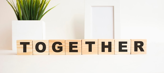 Wooden cubes with letters on a white table. The word is TOGETHER. White surface with photo frame and house plant