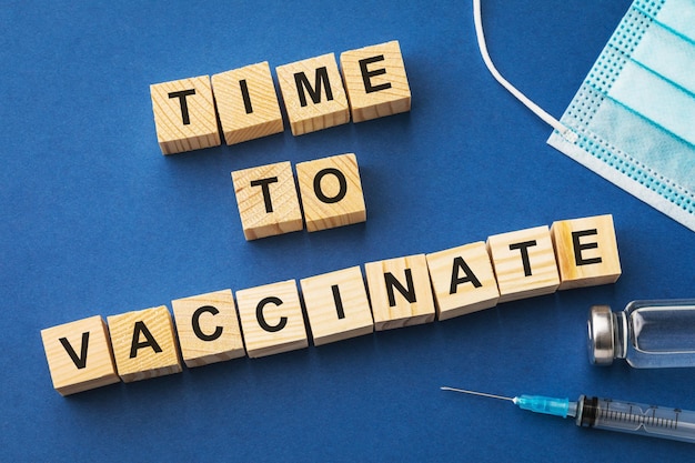 Wooden cubes with text and medical supplies on blue background, time to vaccinate concept