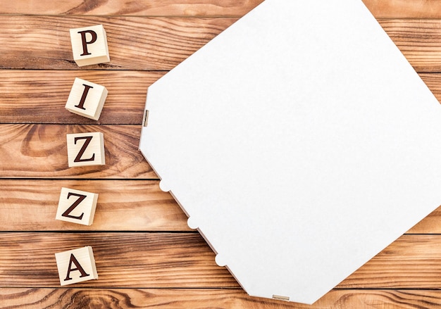 Wooden cubes with word pizza and pizza box on wooden table Top view