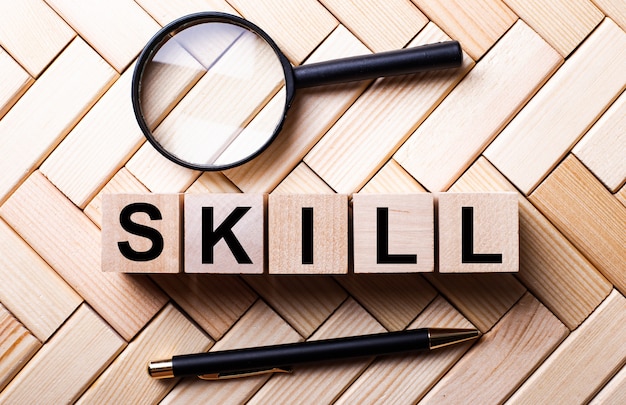 Wooden cubes with the word SKILL stand on a wooden wall between a magnifying glass and a handle