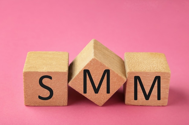 Wooden cubes with word SMM on pink background.