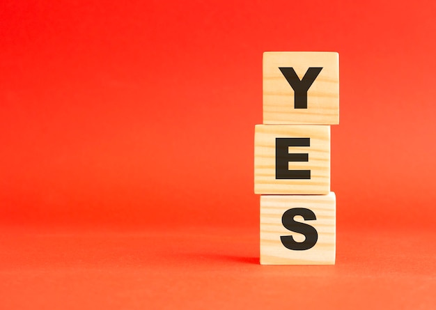 Wooden cubes with word YES. Wooden cubes on a red table. Free space on the left.