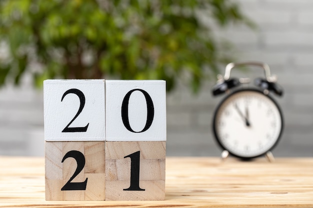 Wooden cubes with year 2021 and alarm clock on working table