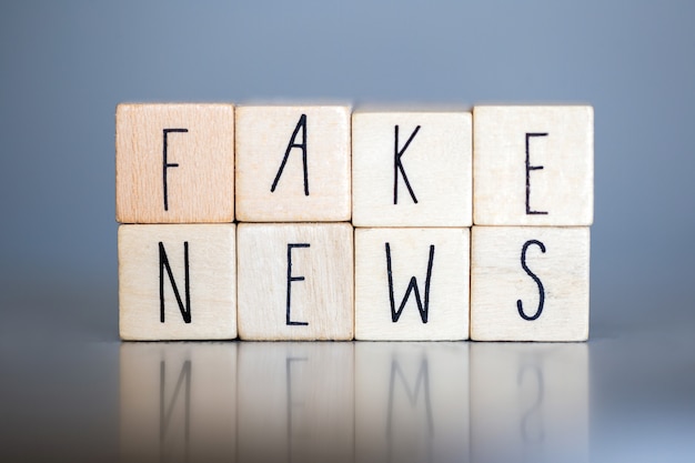 Деревянная кубинка со словами Fake News на серой стене, концепция Fake News в социальных сетях