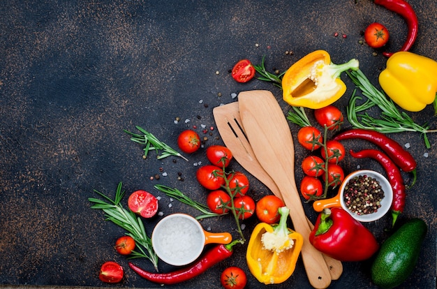 Posate in legno, verdure fresche, spezie, erbe aromatiche e ingredienti sani su sfondo scuro vista dall'alto