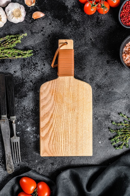 Wooden cutting board  in center of Fresh raw greens, vegetables. Healthy, clean eating, vegan, dieting food concept. Black background. Top view. Copy space