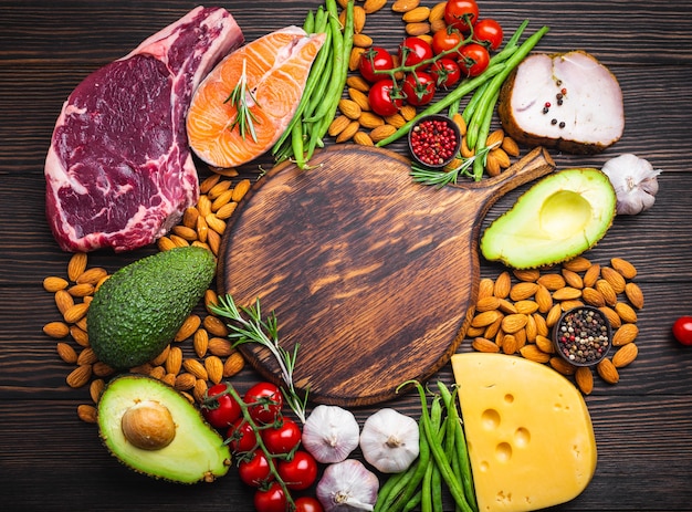 Wooden cutting board and ketogenic low carbs ingredients for healthy weight loss diet, top view, copy space. Keto foods: meat, fish, avocado, cheese, vegetables, nuts. Clean eating, healthy fats