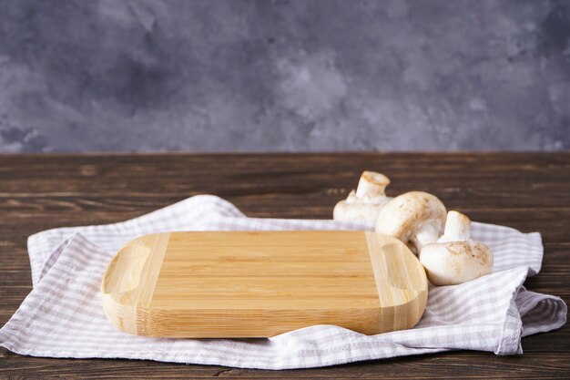 Wooden cutting board and mushrooms on a wooden background, place for text.