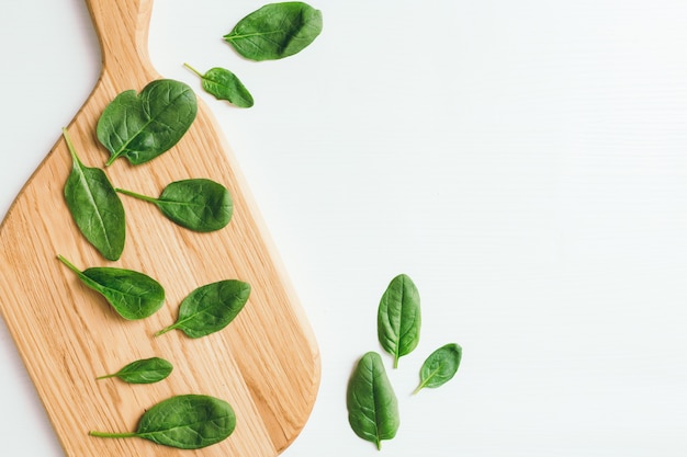 ほうれん草の新鮮な緑のサラダの葉と白い背景の上の木製まな板。健康的な食事の概念