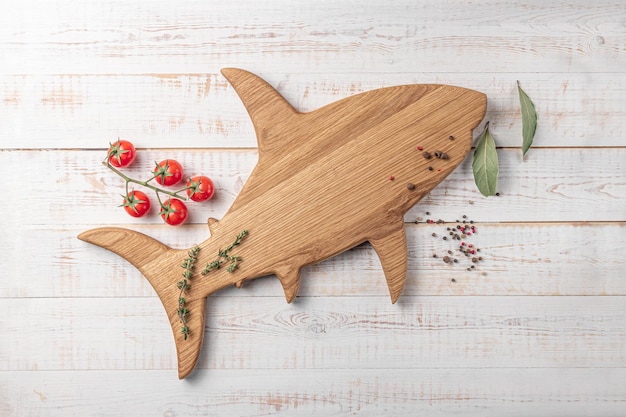 Wooden cutting board shaped fish or shark with cherry tomatoes and spices on a white background mockup with copy space for text top view