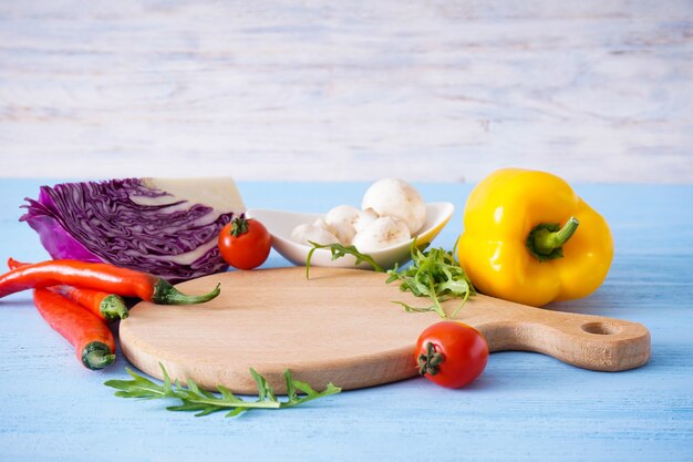 Wooden cutting board and veggies on wooden table, place for text.