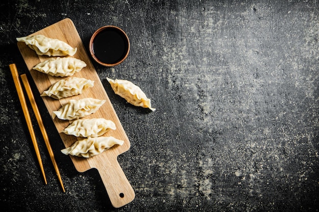 A wooden cutting board with dumplings on it and a saucer with soy sauce on it.