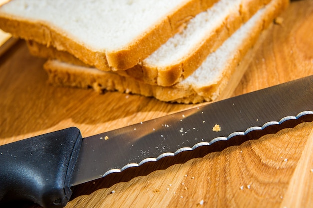 Wooden cutting board with sliced white bread and knife on wooden table